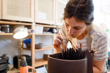 Çömlek atölyesinde çiğ seramik vazo ve kilden esrar yapan bir kadın. Doğal ışık kazıma, düzleştirme, şekillendirme ve yontma ile çömlek atölyesi. Kil tenceresi yapmak