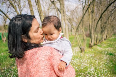 Mutlu anne ve kız bebek, kırsal kesimdeki bir ağacın altında sevgi ve şefkat ile gülümsüyorlar. Aile bağlarının ve olumlu duyguların mükemmel bir portresi. Annelik ve büyüme kavramı