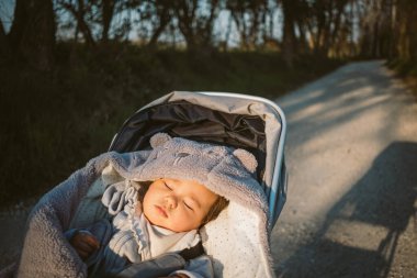 Bebek arabasında huzur içinde uyuyor ya da gün batımında açık havada bebek arabasında. Dışarıdaki sandalyede sakince uyuyan çocuk portresi. gündüz uykusu ve sağlık konsepti yararları