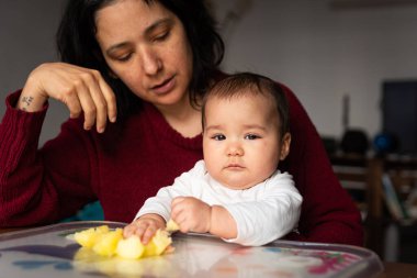 Anne ve bebeğin portresi masada oturuyor ve onu yemek ve meyveyle besliyordu. Kapat. Bebeği emzirme ve emzirme konsepti. İspanyol ailesi.