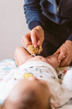 Yatakta bebek bezi değiştiren genç babanın ellerini dikey olarak evde, yatakta bebek kızına yakın tut. Modern bir ailede günlük hayatın ayrıntıları