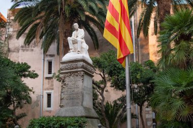 İspanya 'nın Sitges kasabasında, Casa de la Vila olarak bilinen Ajuntament' in tarihi binasında, gün batımında dramatik bir ışıkla birlikte katalan bayrağı bulunan heykel manzarası.