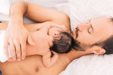 Genç, mutlu bir baba ve yeni doğmuş bebeğiyle şefkatli bir baba gibi yatakta yatıyor.