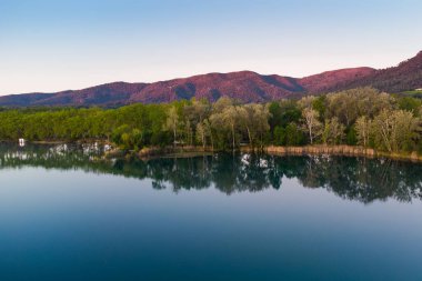 Girona, Katalonya, İspanya 'da gün doğumunda Banyoles Gölü' nün havadan görünüşü. Sabahları huzurlu göl manzarası ve alacakaranlıkta sıcak bir ışıkla çekilen İHA çekimi.