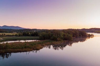 Girona, Katalonya, İspanya 'da gün doğumunda Banyoles Gölü' nün havadan görünüşü. Sabahları huzurlu göl manzarası ve alacakaranlıkta sıcak bir ışıkla çekilen İHA çekimi.