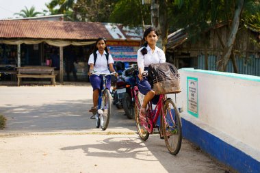 Sundarbans, Hindistan - 2 Kasım 2023: Hindistan 'ın kırsal kesimlerinde okula bisikletle giden Hintli kız öğrenciler. Kendini adamış Hintli kadın öğrencilerin eğitim ve velayet hakkı kavramı