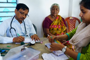 Kolkata, Hindistan - 29 Ekim 2024: Hintli bir doktor Hindistan 'ın kırsal kesimindeki bir klinikte yaşlı bir kadına danışmanlık ve reçete ederken görülüyor.