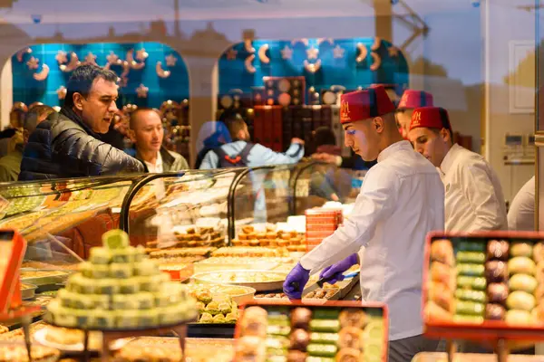 İstanbul, Türkiye - 15 Mayıs 2023: Geleneksel Türk elbiseli pastane yardımcıları baklavalar, Türk tatlıları ve geleneksel Türk tatlılarıyla müşterilere hizmet ederken görülüyor