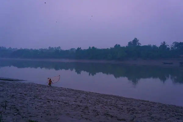 stock image A woman is seen fishing at dusk in a water channel in the Sundarbans mangroves forest in India. Calm and serene landscape of rural India