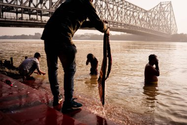 Kolkata, India - 3 November 2023: People are seen performing morning pujas in the Hooghly river with the Howrah bridge in the background in the morning at sunrise. Indian religious ritual clipart