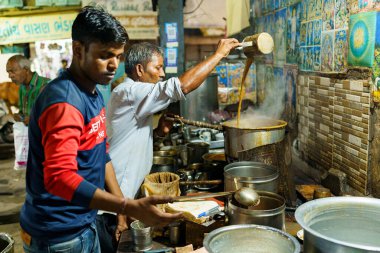 Ahmenabad, India - 20 October 2023: a street chai seller is seen selling chai at night. Old indian man doing informal job, concept of livelihood in indian economy clipart