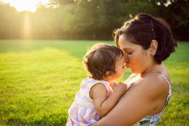 Parkta gün batımında genç bir anne oynuyor ve kızını öpüyor. Annelik ve annelikte uyum kavramı, kaliteli zaman paylaşımı, kopyalama alanı