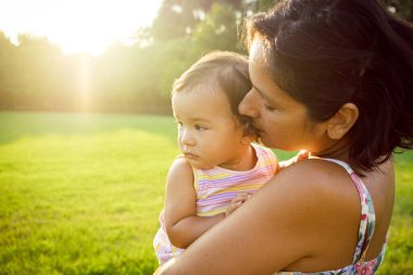 Genç bir anne, gün batımında doğada sevimli küçük kızına sarılıyor ve aynı yöne bakıyor. Annelik ve annelikte uyum kavramı, kaliteli zaman paylaşımı