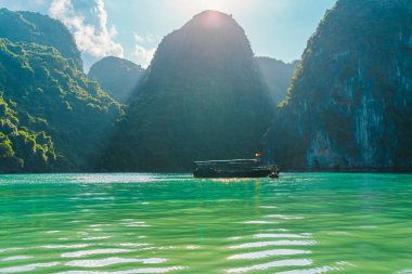 Geleneksel Vietnamlı balıkçı teknesi Ha Long körfezinde güneş ışınlarıyla dağların arasındaki el değmemiş mavi sularda yüzüyor. Ha Long Bay unesco 'nun rüya gibi manzarası ve turistik bir yer..