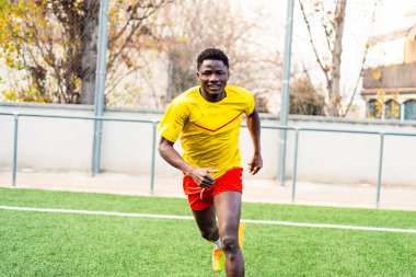 Futbol sahasında antrenman yaparken mutlu görünen gülümseyen siyah Afrikalı bir adamın portresi. Futbol sahasında spor ve egzersiz yapan genç bir sporcu
