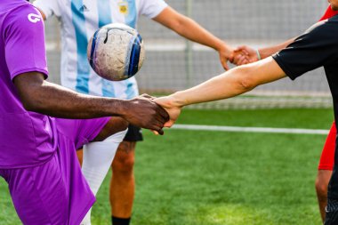 Afrikalı siyah-beyaz melez takım üyelerinin bir spor sahasında el sıkışması. Sporda çeşitlilik ve arkadaşlık kavramı
