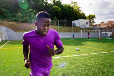 Futbol sahasında koşan ve oynayan gülümseyen siyah Afrikalı bir adamın portresi, mutlu görünüyor. Genç bir sporcu futbol sahasında antrenman yapıyor ve takımla spor yapıyor.