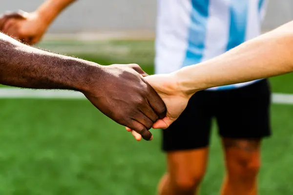 Afrikalı siyah-beyaz melez takım üyelerinin bir spor sahasında el sıkışması. Sporda çeşitlilik ve arkadaşlık kavramı