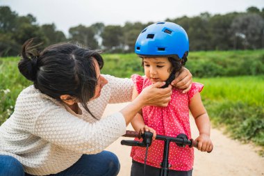 Genç milenyum annesi, kask takan küçük kıza dışarıda bisiklet sürmeyi öğrenmesinde yardım ediyor. Büyüyen ve gelişen bebek kavramı, anne kızının açık havada birbirine bağlanması.