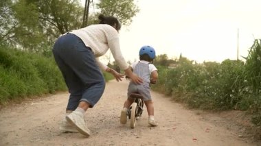 Mutlu anne, kızına dışarıda bisiklet sürmeyi öğrenmesinde yardım ediyor. Şirin çocuk, çocuklarla bisiklete biniyor. Annelik ve anne kız bağı kavramı