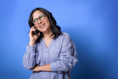 40 'lı yaşlarda genç İspanyol bir kadın cep telefonuyla konuşuyor, sohbet ederken gülümsüyor, stüdyo portresi çekiyor.