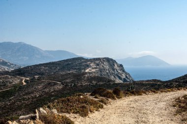 Denizin arka planında dağlar olan bir yol..