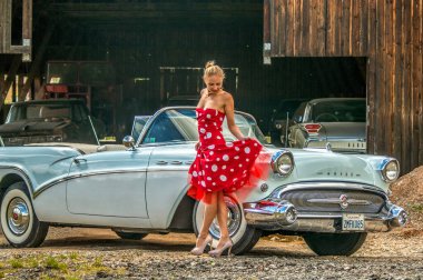 Güzel bir esmer model klasik bir arabada poz verirken dışarıda poz veriyor.