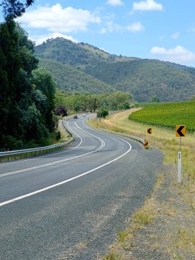 Avustralya 'nın kırsal kesimindeki dikey dağ yolu, ağaçlar ve araba tabelası