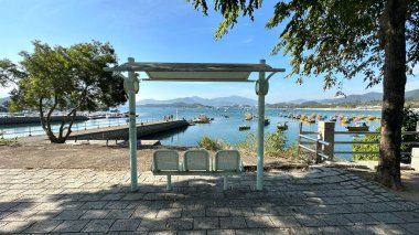 Mavi sandalyeler, patika, Hong Kong açıkhava parkı mavi gökyüzü ve gölde eğlence tekneleri olan ağaç.