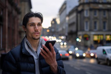 Newcastle 'da bir caddede duran genç bir adam akşamleyin Tyne' ın tepesinde cep telefonuyla bir arkadaşıyla konuşurken. Taksiyi bekliyor..