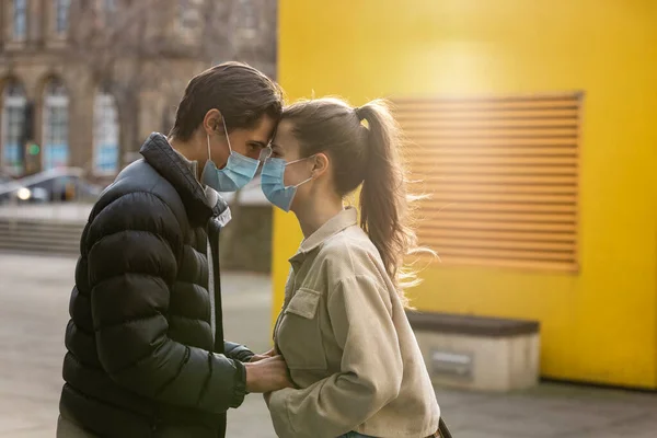 stock image A young couple spending the day in Newcastle Upon Tyne. They are standing on a paved area in the city centre while holding hands and putting their heads together. They are wearing protective masks.