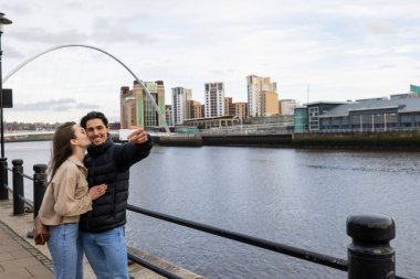 Bir araya gelip öpüşen ve selfie çeken genç bir çiftin geniş açılı görüntüsü. Birbirlerine aşıklar..