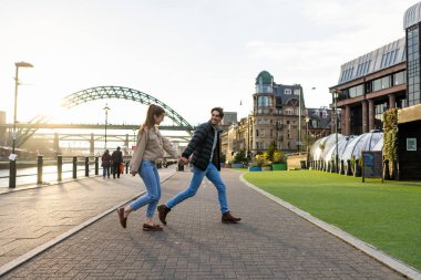 Yan yana yürüyen genç bir çiftin yan görüntüsü. El ele tutuşuyorlar ve birbirlerine aşıklar..