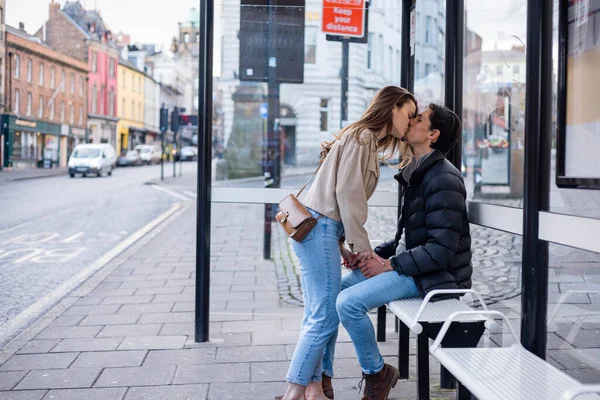 バスの停留所で一緒に待っている若いカップルの横ビューショット 彼らは愛にあり キスを共有 — ストック写真