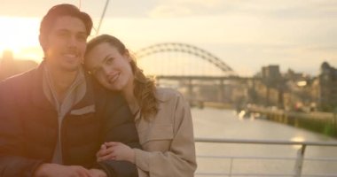 Genç bir çift günü Tyne 'da Newcastle' da birlikte geçiriyorlar. Köprüde duruyorlar ve arkalarında Tyne nehri var. Birbirlerine sarılıp öpüşüyorlar..