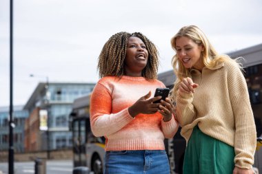 İngiltere 'nin Newcastle kentindeki bir caddede duran iki yetişkin kadının ön görüntüsü. Akıllı telefon kullanırken yol tarifi arıyorlar. Günlük giysiler giyiyorlar ve ne tarafa gideceklerini tartışıyorlar..