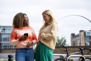 İngiltere 'nin Newcastle kentindeki bir caddede duran iki yetişkin kadının ön görüntüsü. Akıllı telefon kullanırken yol tarifi arıyorlar. Günlük giysiler giyiyorlar ve ne tarafa gideceklerini tartışıyorlar..