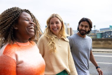 İngiltere, Newcastle 'da bir caddede yürüyen üç yetişkin arkadaşın yan görüntüsü. Günlük giysiler giyiyorlar ve yan yana yürüyorlar, gülümsüyorlar ve sohbet ediyorlar..