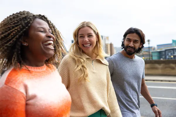 İngiltere, Newcastle 'da bir caddede yürüyen üç yetişkin arkadaşın yan görüntüsü. Günlük giysiler giyiyorlar ve yan yana yürüyorlar, gülümsüyorlar ve sohbet ediyorlar..