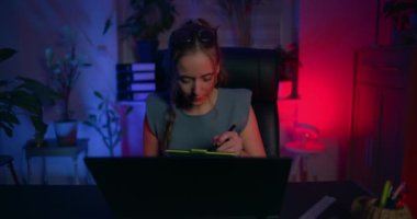 Odaklanmış bir kadın dizüstü bilgisayarının önünde oturuyor ve kendini bilişim programcısı olarak işine veriyor..