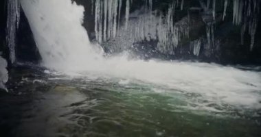 Kış şelalesi bir dağdan aşağı akar, tatlı su ve karla kaplı dağların manzarası ve buzlu ağaçlar, huzurlu ve sakin bir atmosfer yaratır..