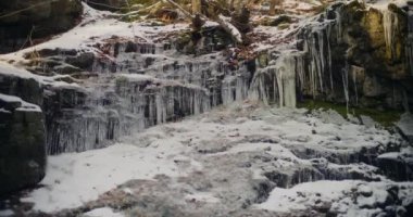 Kış şelalesi bir dağdan aşağı akar, tatlı su ve karla kaplı dağların manzarası ve buzlu ağaçlar, huzurlu ve sakin bir atmosfer yaratır..