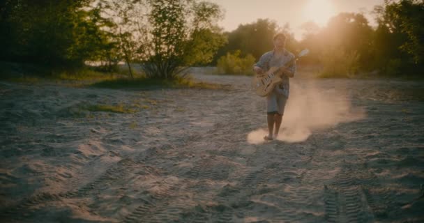 輝く太陽の下で 若い喜びに満ちたギタリストは 彼が彼のギターを鳴らすと純粋な至福を見つけ ビーチの穏やかな雰囲気を受け入れながら音楽の調和の中で明らかにします — ストック動画