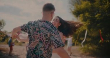 Kumsalda yaz hafta sonu partisinin tadını çıkarırken erkek arkadaşıyla dans eden sırıtan esmer bir kadın.