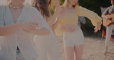 Dans eden ve plajda arka planda erkeklerle müzik dinleyen genç bayan arkadaşların orta kesimi.