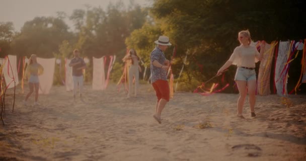 夕暮れ時に友達がビーチに群がっている間 若いカップルの踊りの完全な長さ — ストック動画