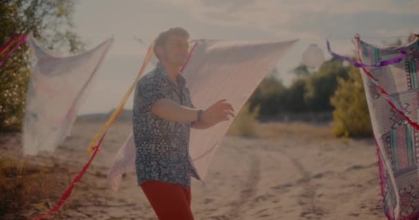 Улыбающийся Молодой Человек Наслаждается Музыкой Играя Против Саронгов Висящих Пляже — стоковое видео