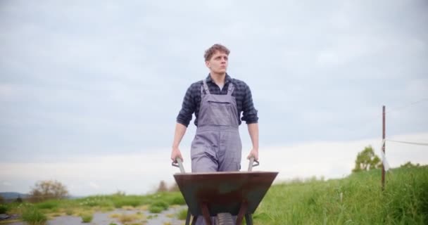 Çiftlikte Yürürken Arabasını Iten Kendinden Emin Genç Çiftçinin Yavaş Hareketi — Stok video