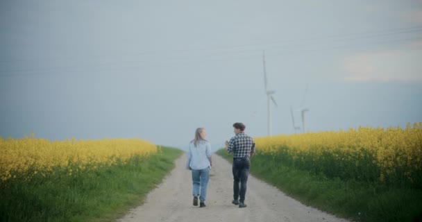 农民在农场黄花丛中行走时与农艺师交谈的后视镜 — 图库视频影像