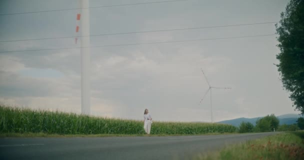 女子在风电场附近的路边与天空相对的慢镜头 — 图库视频影像